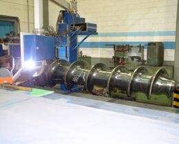 A large screw gets refurbished by welding a hard-facing onto the outside diameter of the flights